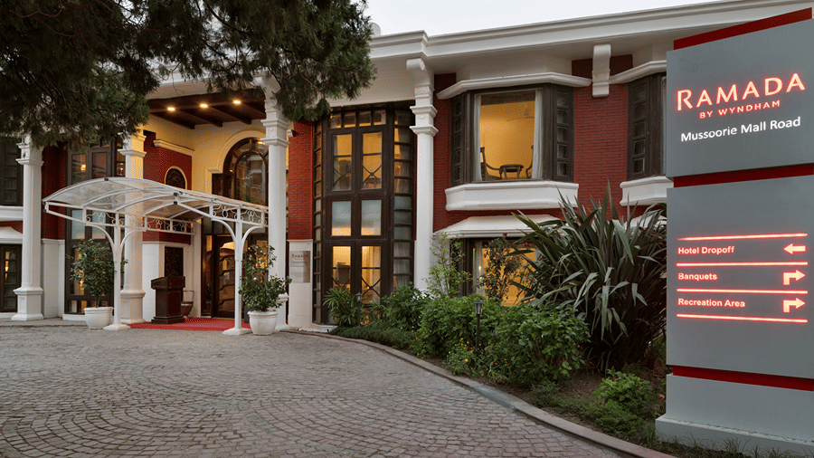 A multi-storey building exterior features a main entrance and a signage board for Ramada by Wyndham Mussoorie Mall Road.