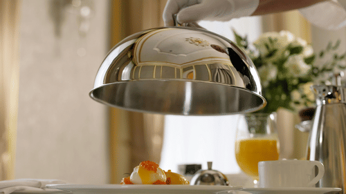 a person lifting a cloche in a hotel room