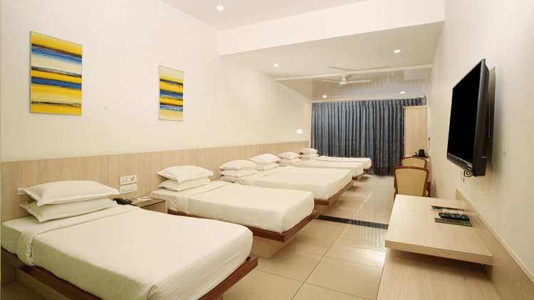 Hotel room interior featuring multiple single beds lined up, a wall-mounted TV, and an air conditioning unit at Arawali Ananta Elite, Jaipur.
