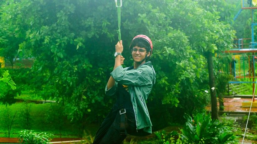 A charming teenager wearing a helmet on a zipline, with the backdrop of a huge tree's canopy