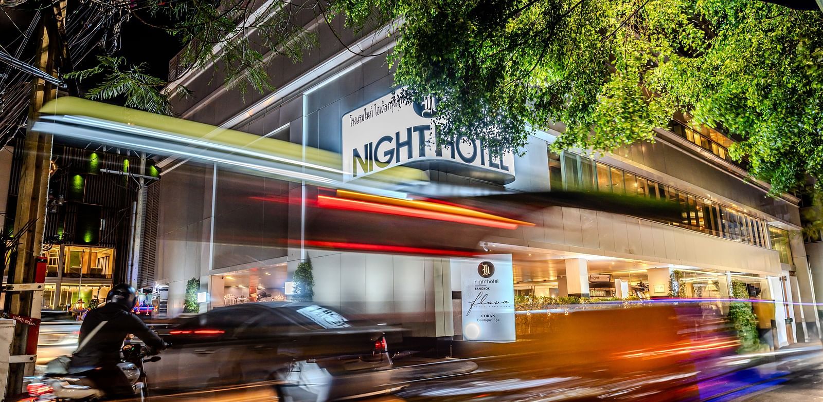 A picture showing Night Hotel Bangkok's Facade with vehicles travelling on the road.