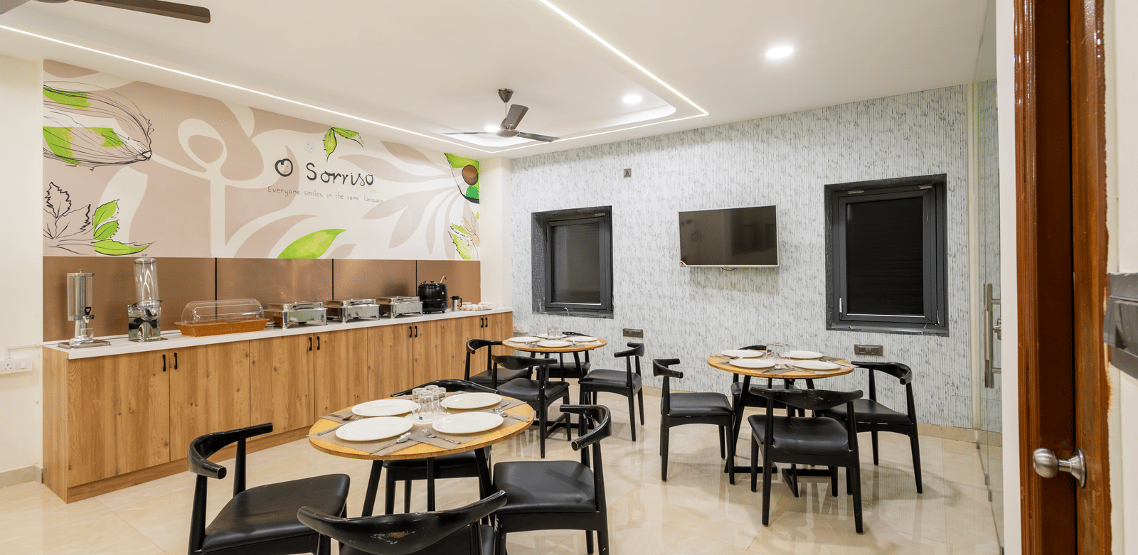 A dining area with tables and chairs at Elysium Studio Suites, Madhapur, has wall decorations and overhead lights.