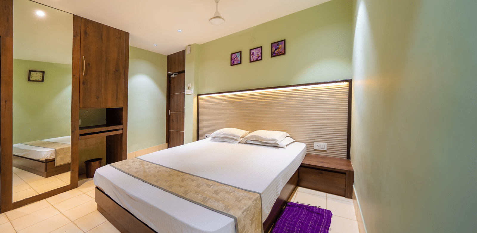 Minimalist room with double bed, wooden furniture, ceiling fan, and framed artworks above the bed – Hotel Dolphin Puri