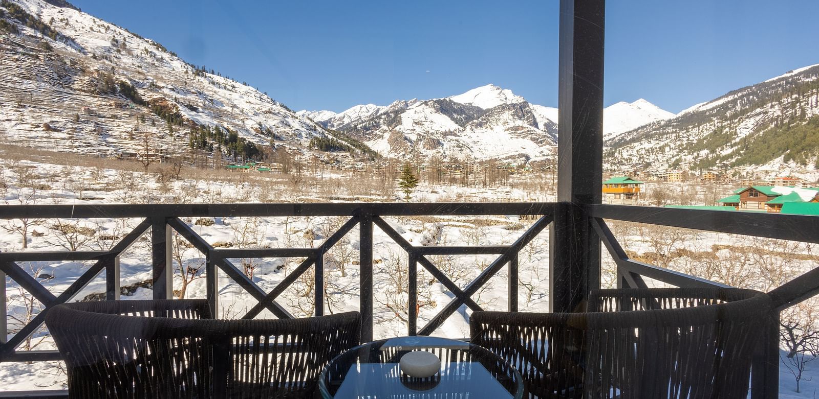 Balcony with chairs and a table overlooking snowy mountains at Nivasana Manali.
