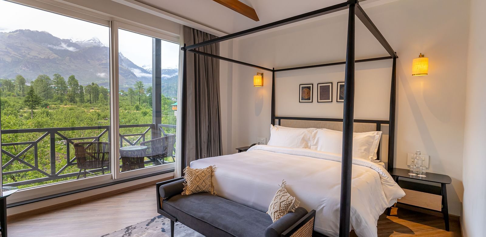 Spacious wooden-framed bed with seating at the foot and a large glass door opening to mountain views at Nivasana Manali.