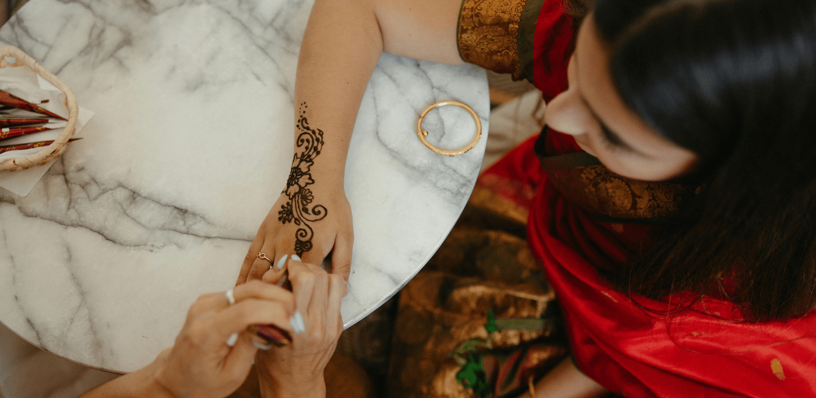 A woman wearing a red saree getting mehendi done on her hands.