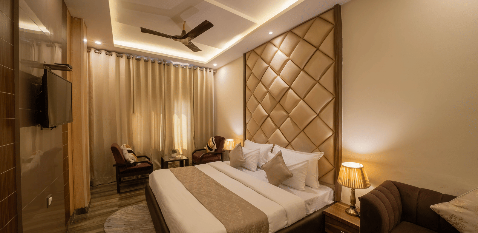 Warmly-lit hotel room with a large bed, ceiling fan, and brown and white decor - Perfectstayz Premium at Har Ki Pauri Road (Ganga Heights)