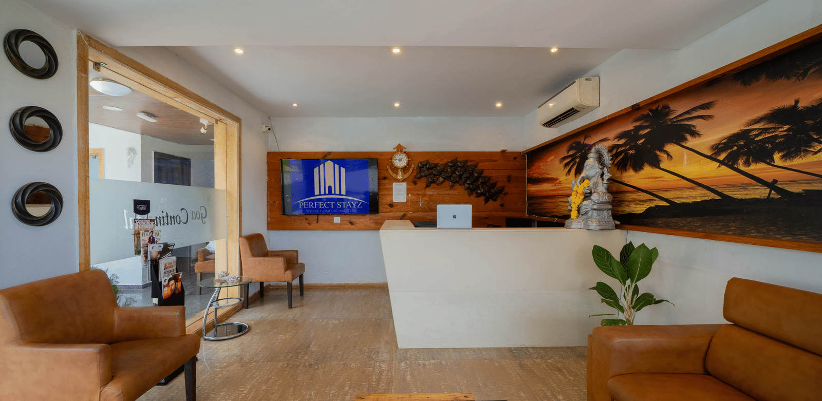 A stylish hotel reception area with a counter, comfortable leather seating, and a decorative beach mural - Perfectstayz Premium Goa Continental