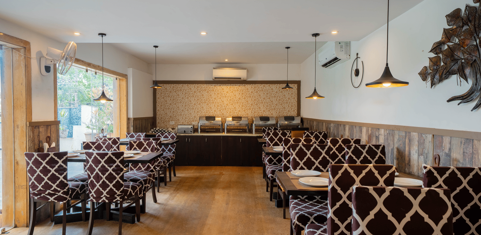 A well-lit, modern dining room featuring a patterned booth seating and wooden flooring at Perfectstayz Premium Goa Continental.