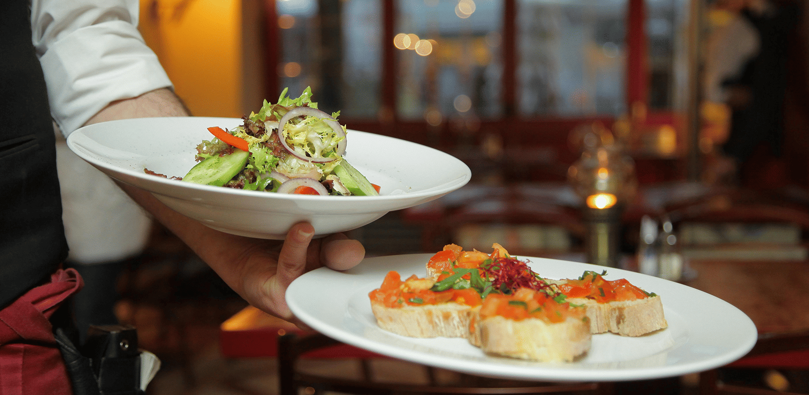 a person in a restaurant holding two plates with delicious cuisines in it that are well plated