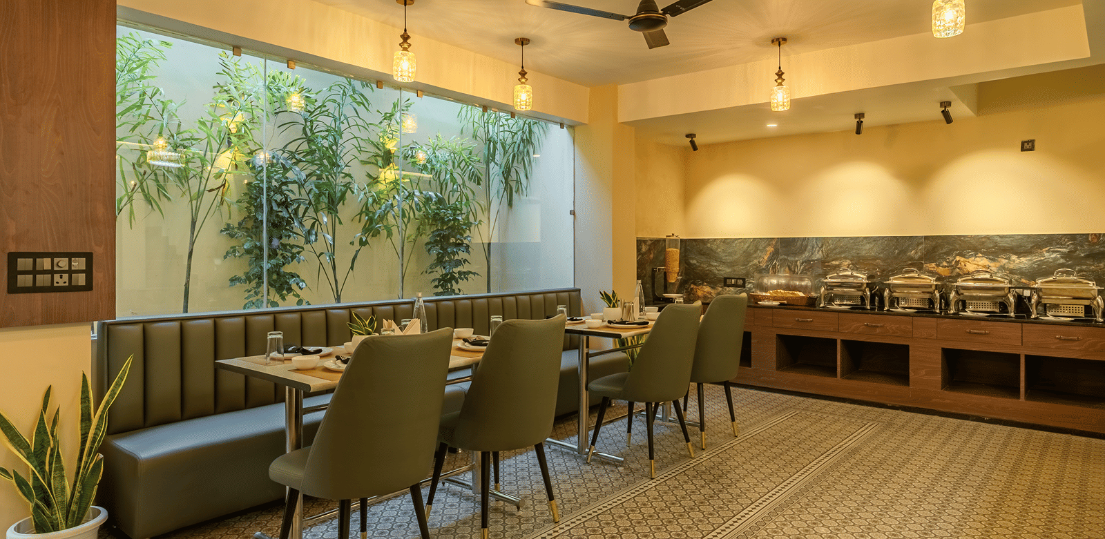 Wide view of the restaurant at Perfectstayz Premium Lavender, Varanasi with green chairs, a banquette, patterned floor tiles, pendant lamps, and a buffet counter.