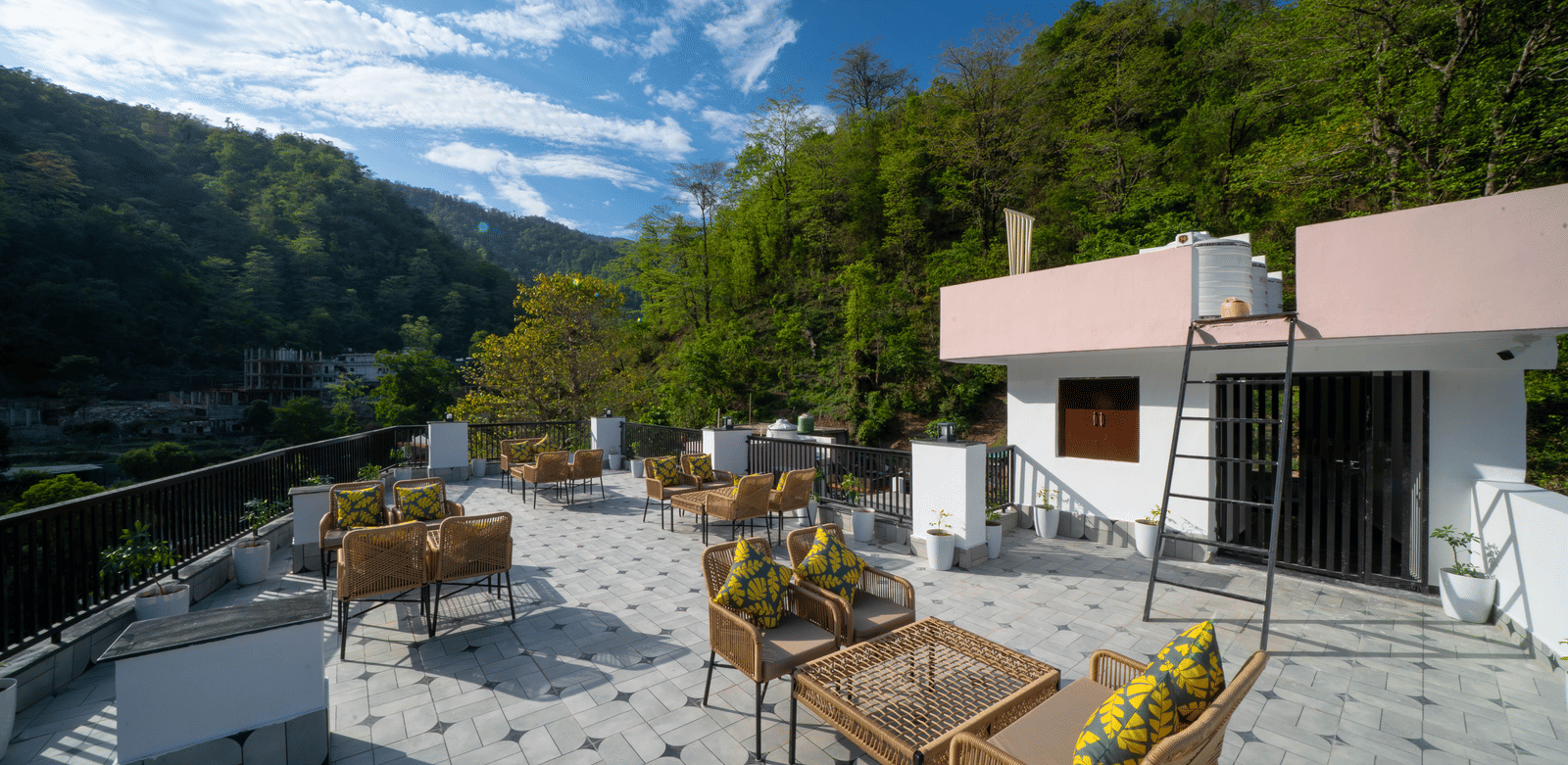 A rooftop terrace with tables, chairs, floor tiles, and a building structure with a flat roof in Perfectstayz Premium Mystic Falls, Rishikesh.
