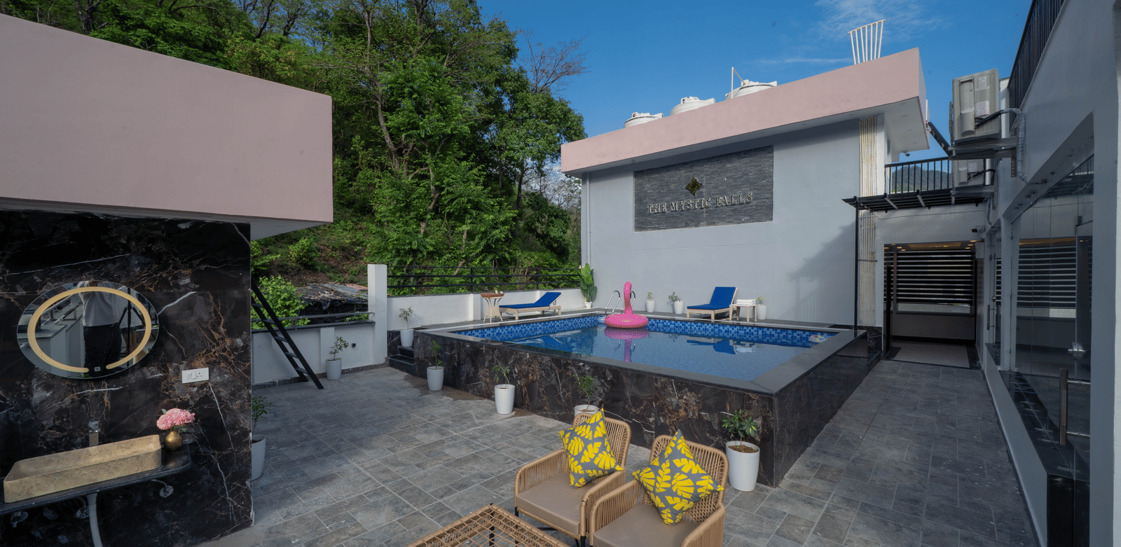 A terrace with a swimming pool, a railing, wicker furniture, and a building exterior visible in Perfectstayz Premium Mystic Falls, Rishikesh.