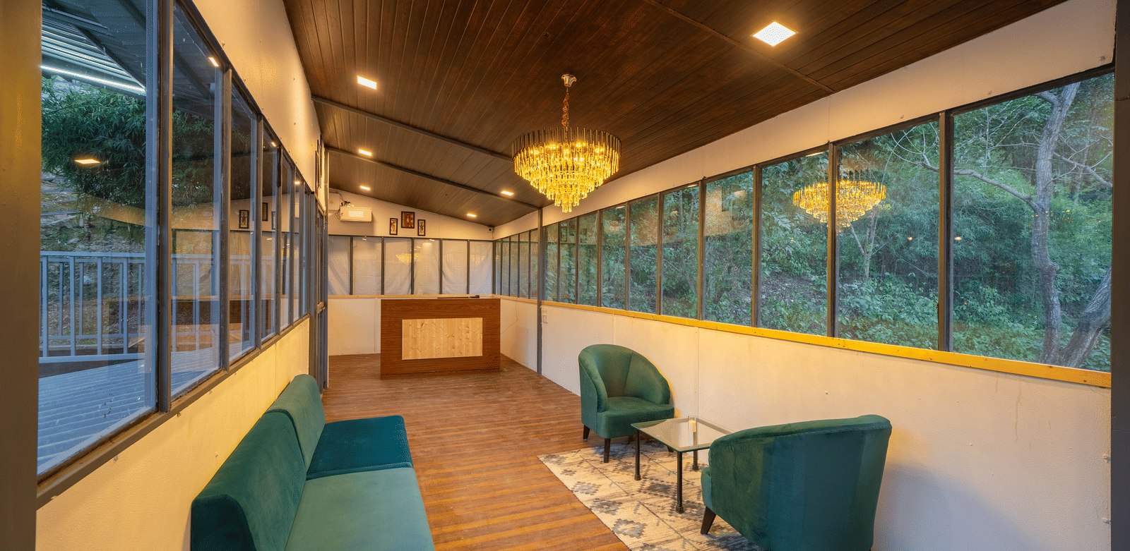 An indoor lounge at Perfect Stayz The Jungle Resort has sofas and a long corridor with windows.