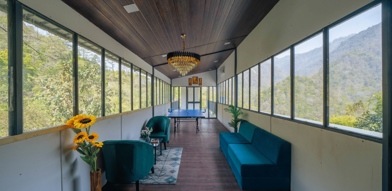An indoor lounge at Perfect Stayz The Jungle Resort has sofas, a long corridor, and windows overlooking the forest.