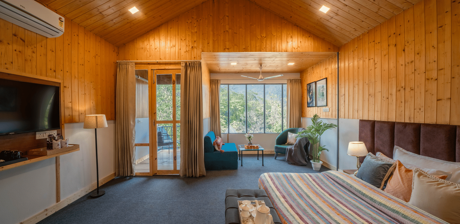 A spacious, wood-paneled room with a vaulted ceiling, a king-size bed, a lounge area, and a large TV.