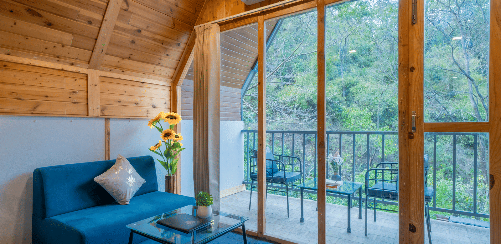 A sitting area at Perfect Stayz The Jungle Resort includes a sofa, a coffee table, and a balcony beyond the glass door.