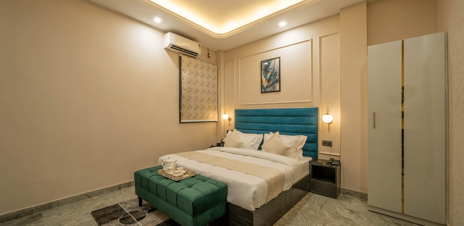 Interior view of a modern bedroom with a white bed, dark green velvet bench, white wardrobe, and ceiling lighting - Perfectstayz Value Aalaya Suites, Haridwar