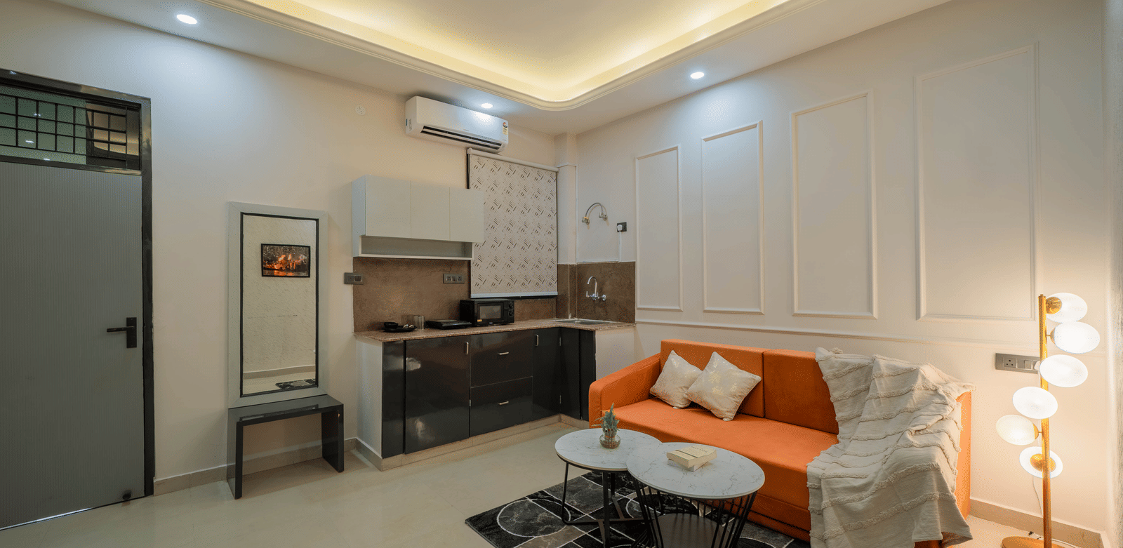 Spacious living area featuring an orange sofa, rug, and a small kitchenette with white cabinetry - Perfectstayz Value Aalaya Suites, Haridwar