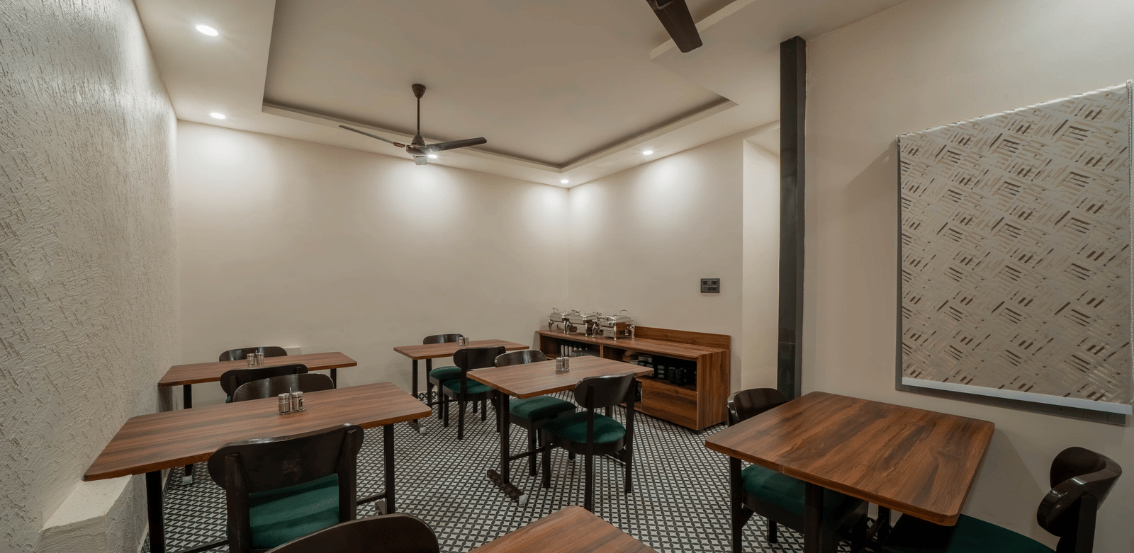 Side view of a dining room with dark wooden tables, chairs, and ceiling fans - Perfectstayz Value Aalaya Suites, Haridwar