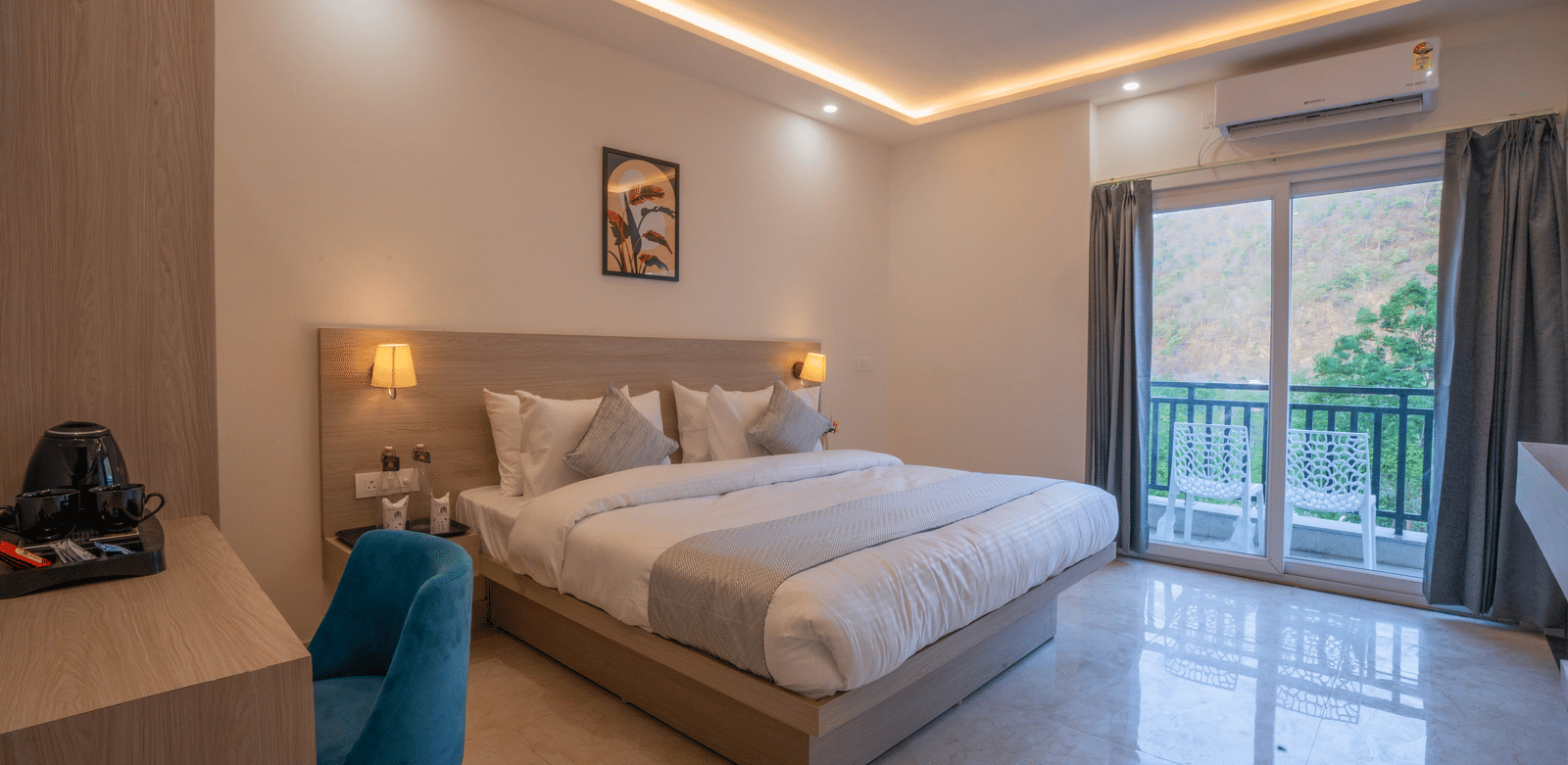 A well-lit, stylish master bedroom at Perfectstayz Value Alpine Retreat, Rishikesh with a large grey bed, dressing table, and sliding glass balcony doors.