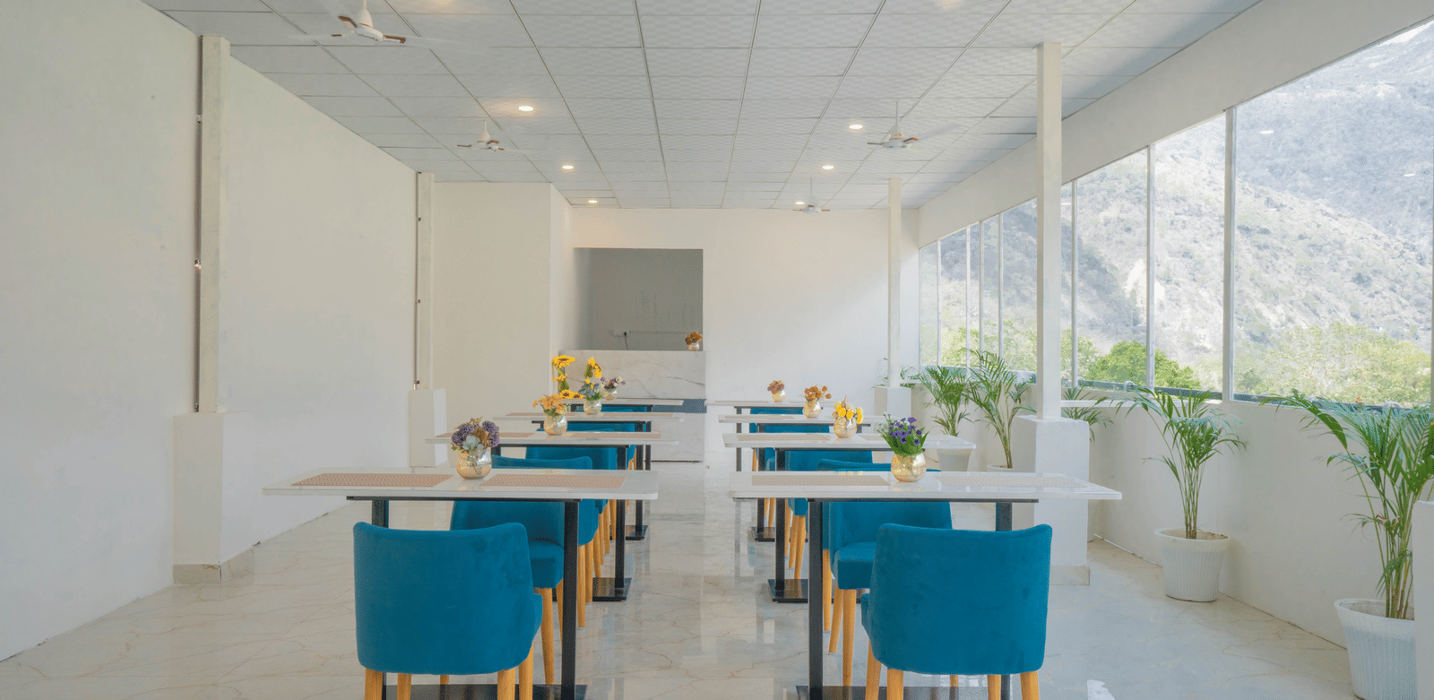A spacious dining hall at Perfectstayz Value Alpine Retreat, Rishikesh with white interiors and neatly arranged chairs and tables.