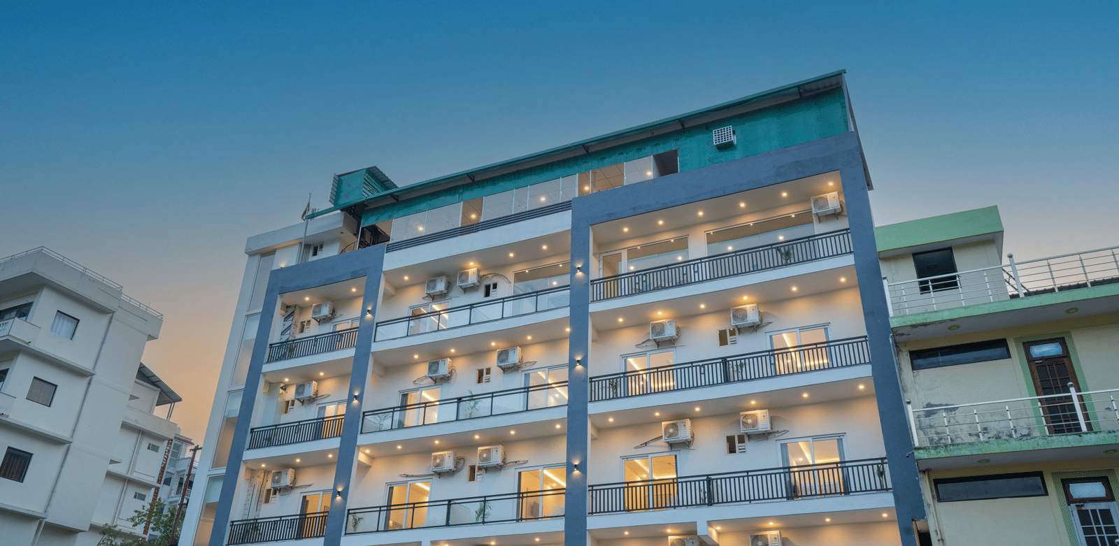 A modern building of Perfectstayz Value Alpine Retreat, Rishikesh with multiple balconies, against a clear blue sky.