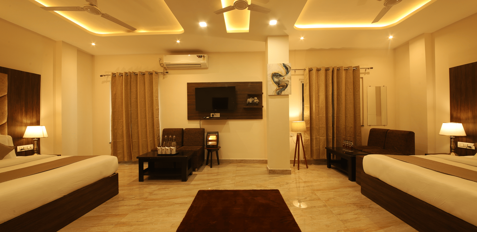 The empty space between the 2 double beds in the Family Room featuring a brown rug in the middle along with a wall-mounted television at the Perfectstayz Value Dhruv Nanda.