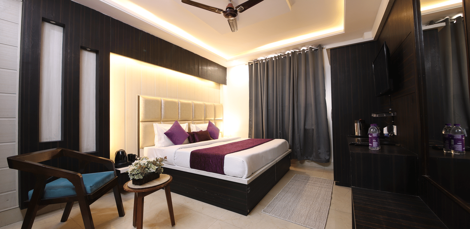 Spacious hotel room with a large bed, modern dark wood furniture, and a seating area with 2 blue chairs - Perfectstayz Value Grey Castle, Haridwar