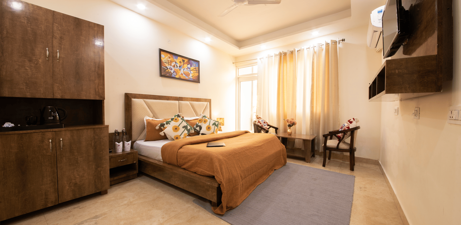 A hotel room, featuring a large bed with a brown duvet and pillows, a dark wooden headboard and nightstands, a ceiling fan, and a wall-mounted TV | Perfectstayz Value Hills