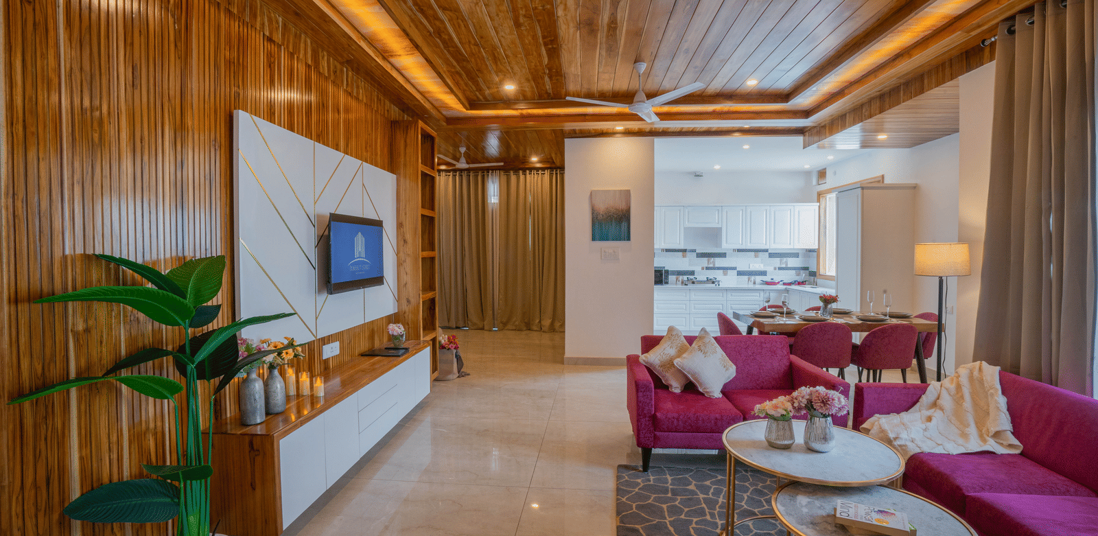 A living area at Perfectstayz Value Paradise, Mussoorie, with wooden walls, a television, a potted plant, a sofa set, 2 coffee tables, and ceiling lights.