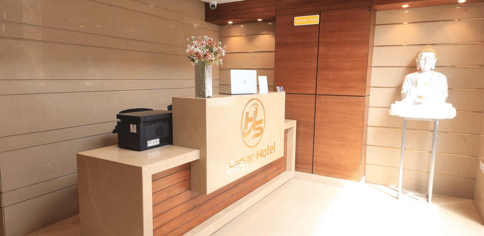 A hotel reception area, featuring a reception desk with a logo, a printer, and a statue on a stand | Perfectstayz Value Sagar