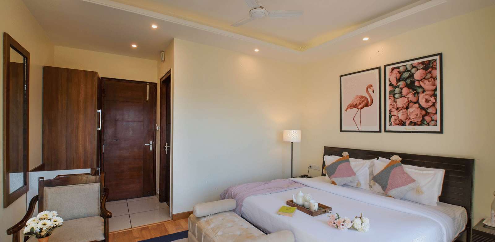 A bedroom at Perfectstayz Value Shimla (Namah Retreat) with a king size bed, 2 chairs, a table, wall art, and a cupboard.