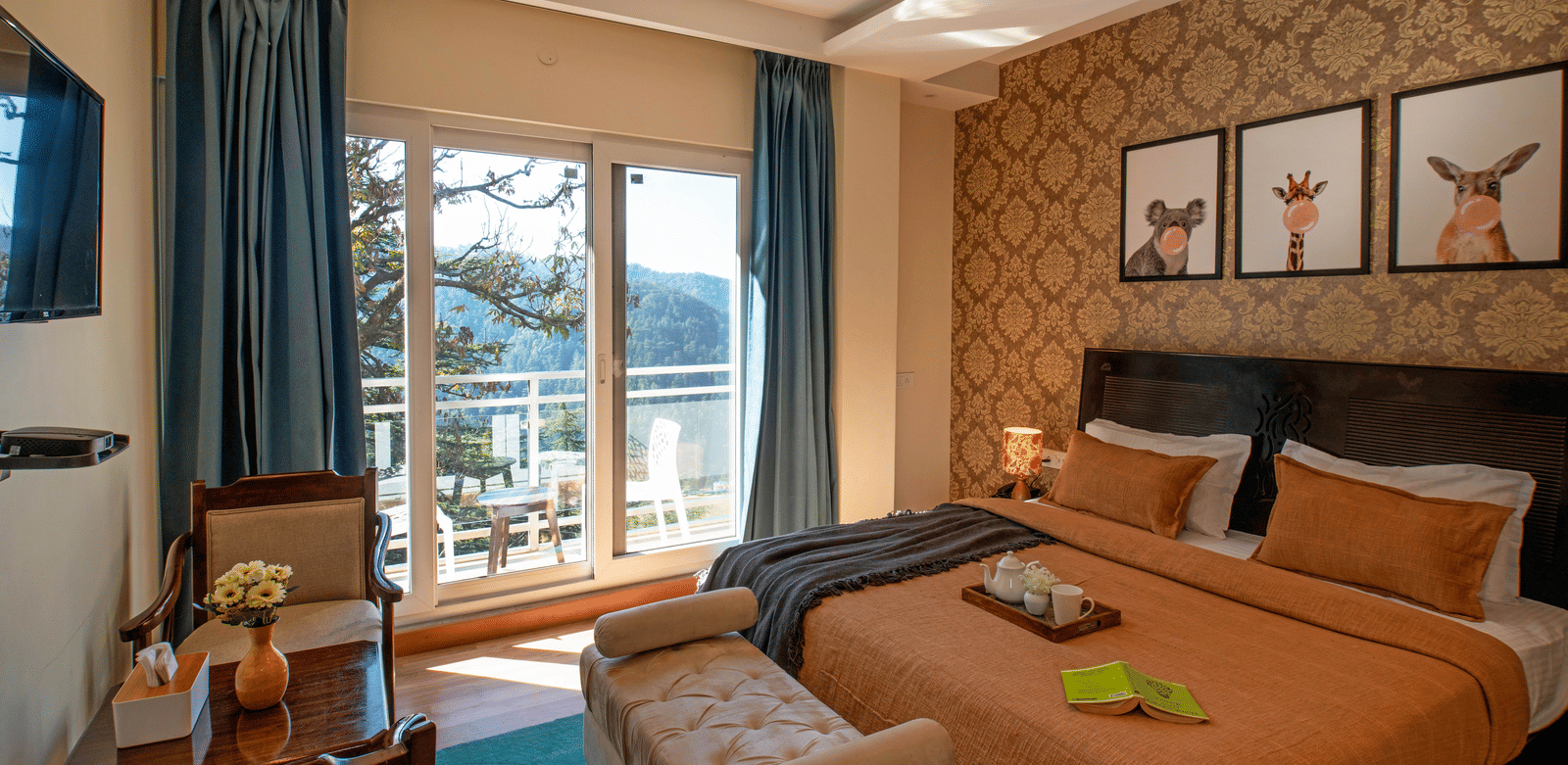 A bedroom at Perfectstayz Value Shimla (Namah Retreat) with a king size bed, wall art, a television, a table, 2 chairs, a daybed, a tray with cups and a kettle, and a sliding door leading to a balcony with a table and chairs.