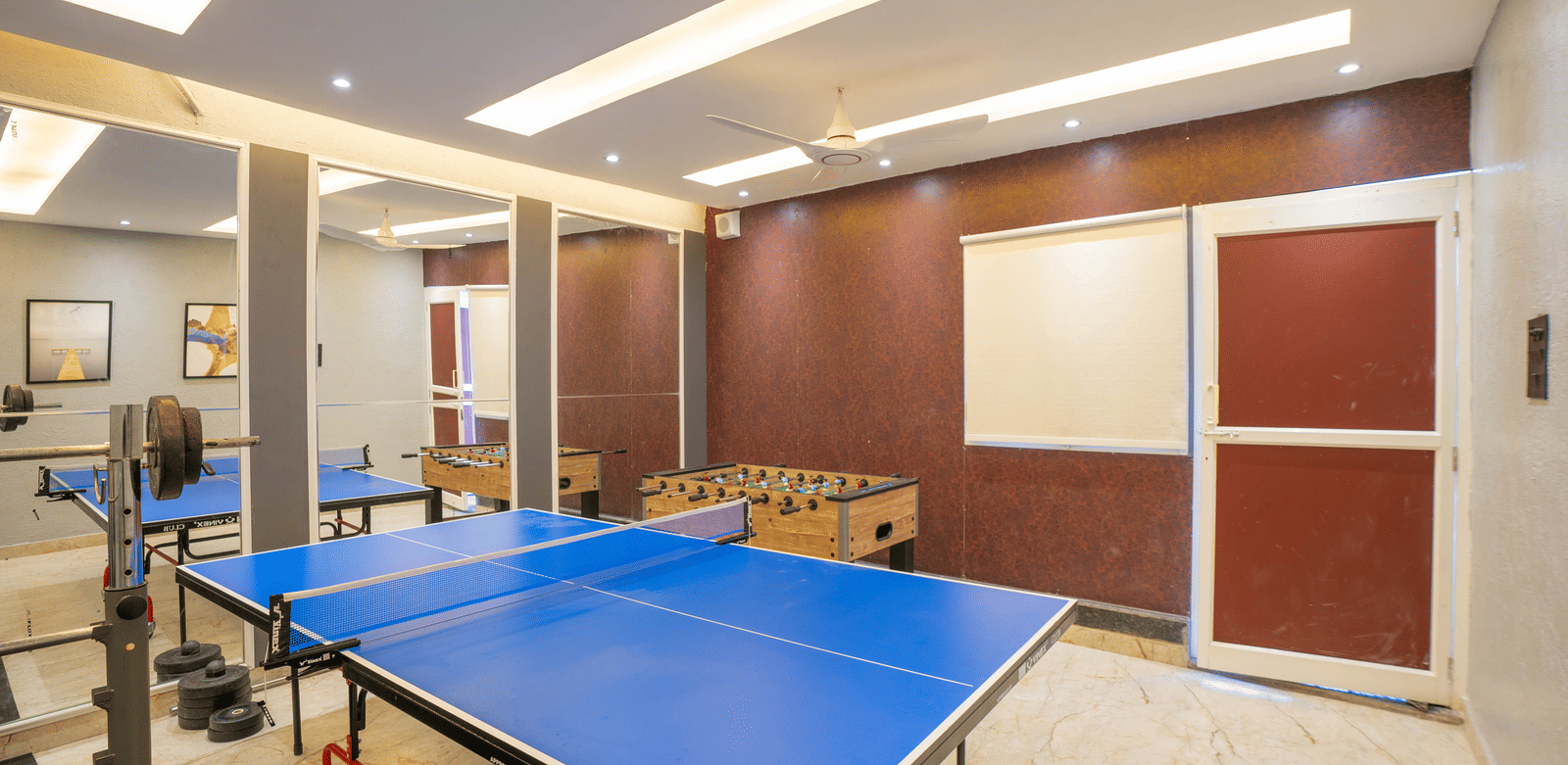 The vibrant games room at Sukoon by the Ganges features a blue table tennis table, a foosball machine, and ample space for activities.