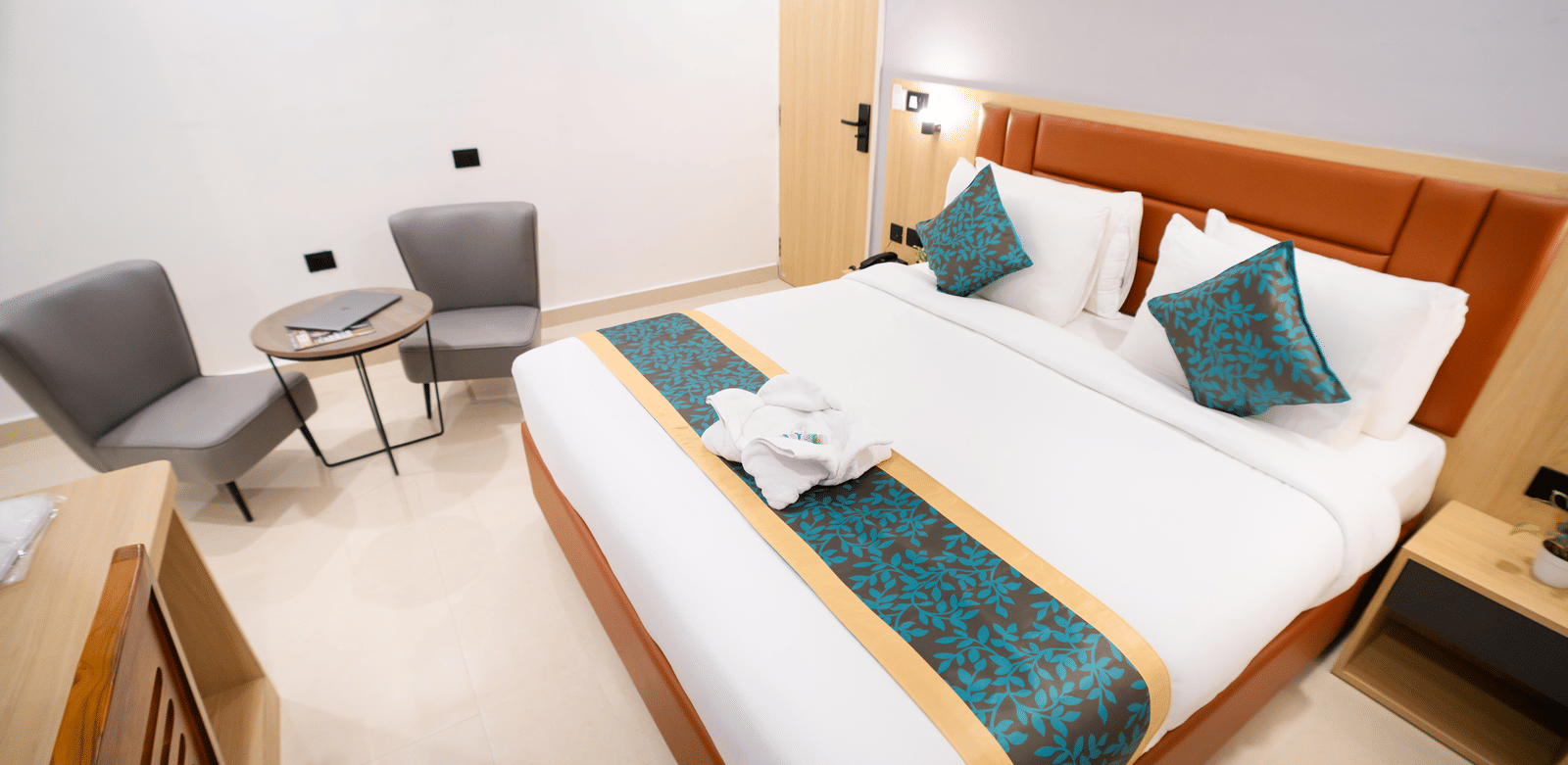 View of a spacious room with a large bed with a headboard, bedside tables on both sides, and a seating area to the side at Sunrise Business Hotel, Hyderabad.