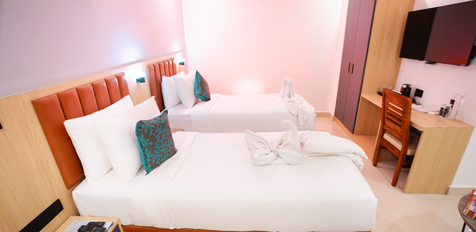 Side view of a spacious room with twin beds, a bedside table, and a wall-mounted television at Sunrise Business Hotel, Hyderabad.