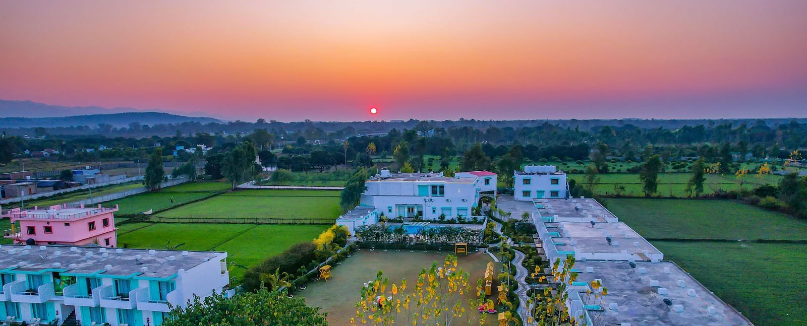 Scenic aerial view of Vedikant Resorts The Mallard Corbett surrounded by fields during a vibrant sunset.