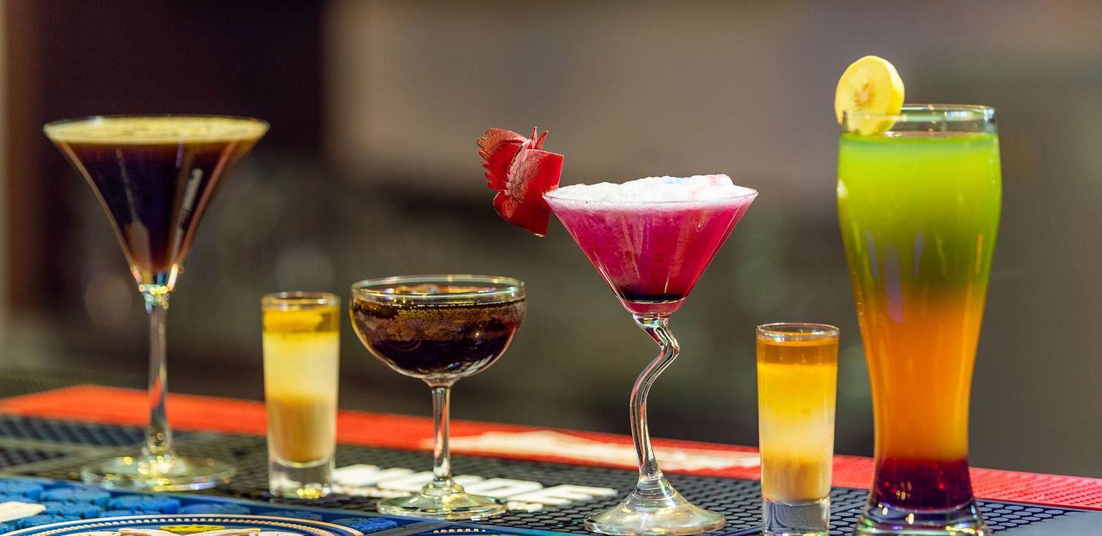 Assortment of colorful cocktails and shot glasses arranged on a bar counter with a blurred background.