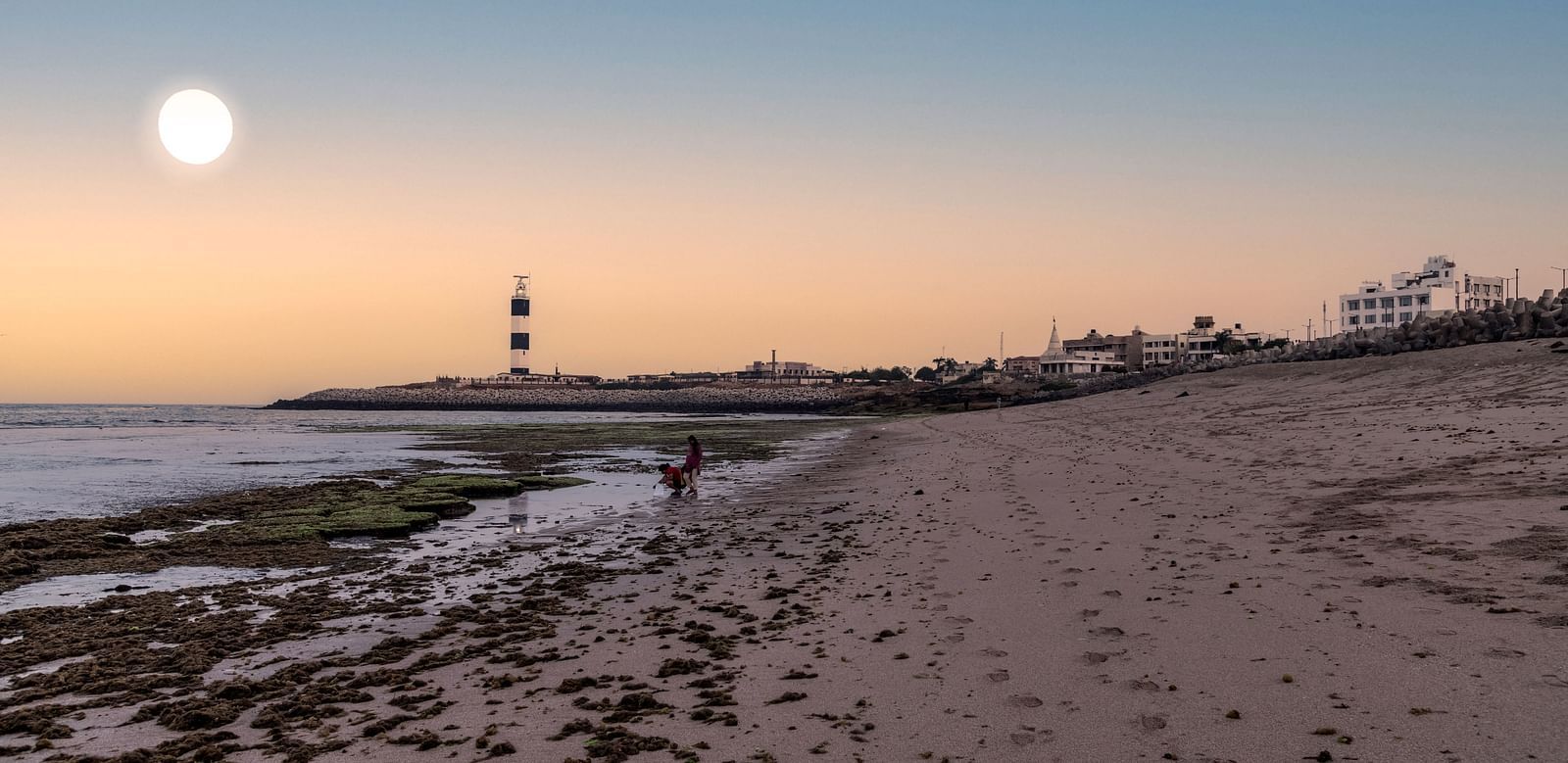 A serene beach scene at dusk with a lighthouse silhouetted against the fading light.