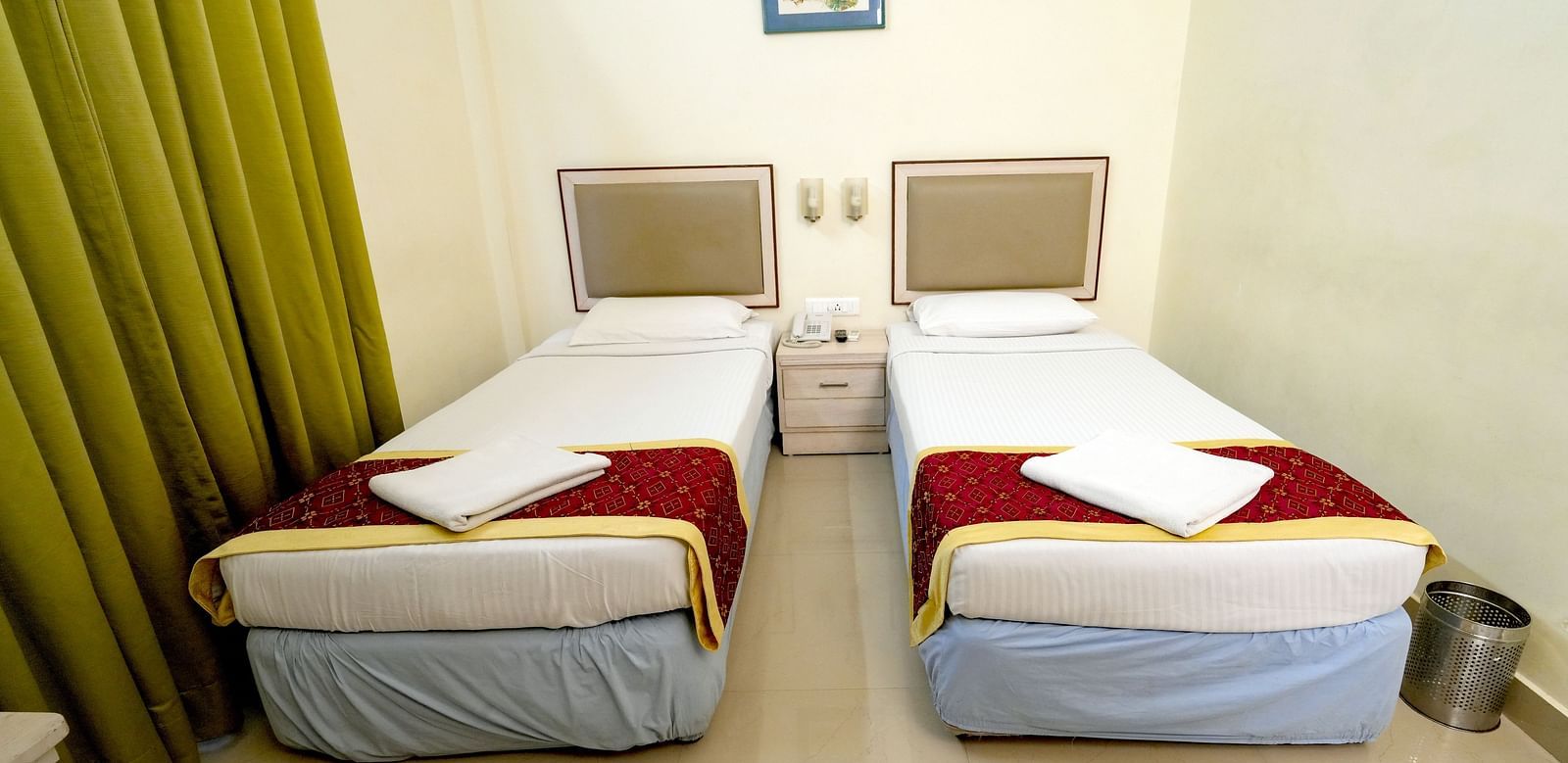A hotel twin bedroom with white and mustard bedding, green curtains, and a picture on the wall at Greens Inn - Comfortable Twin Rooms in Ramoji Film City.