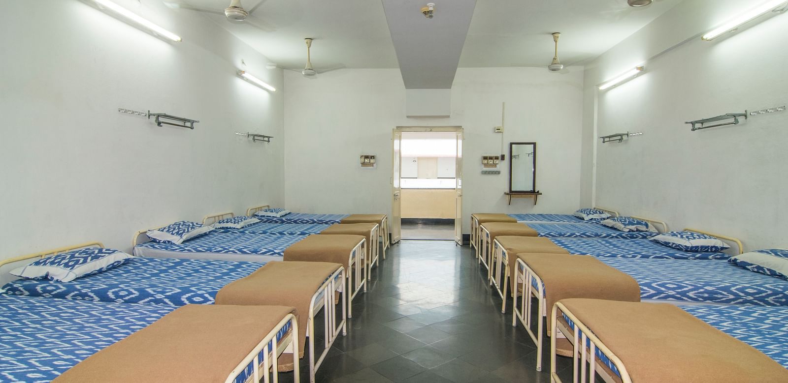 A full view of beds with bedding arranged in two rows in a room | Hotel Sahara