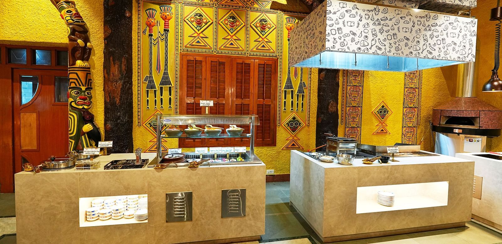 A buffet area with traditional design elements, wood carvings, and ambient lighting at Tara, Comfort Hotel in Hyderabad - Ramoji Film City.