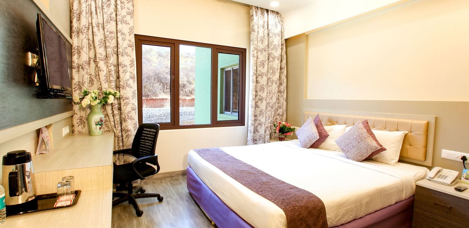 A modern hotel room with a plush king-sized bed and a view of the outdoors. - Tara, Comfort Hotel in Hyderabad - Ramoji Film City.