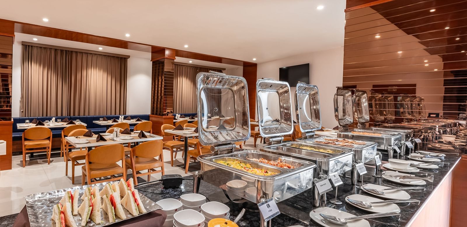 A buffet spread with covered food warmers, plates, and other serving dishes is ready in a dining area - Lords Eco Inn Ambaji.