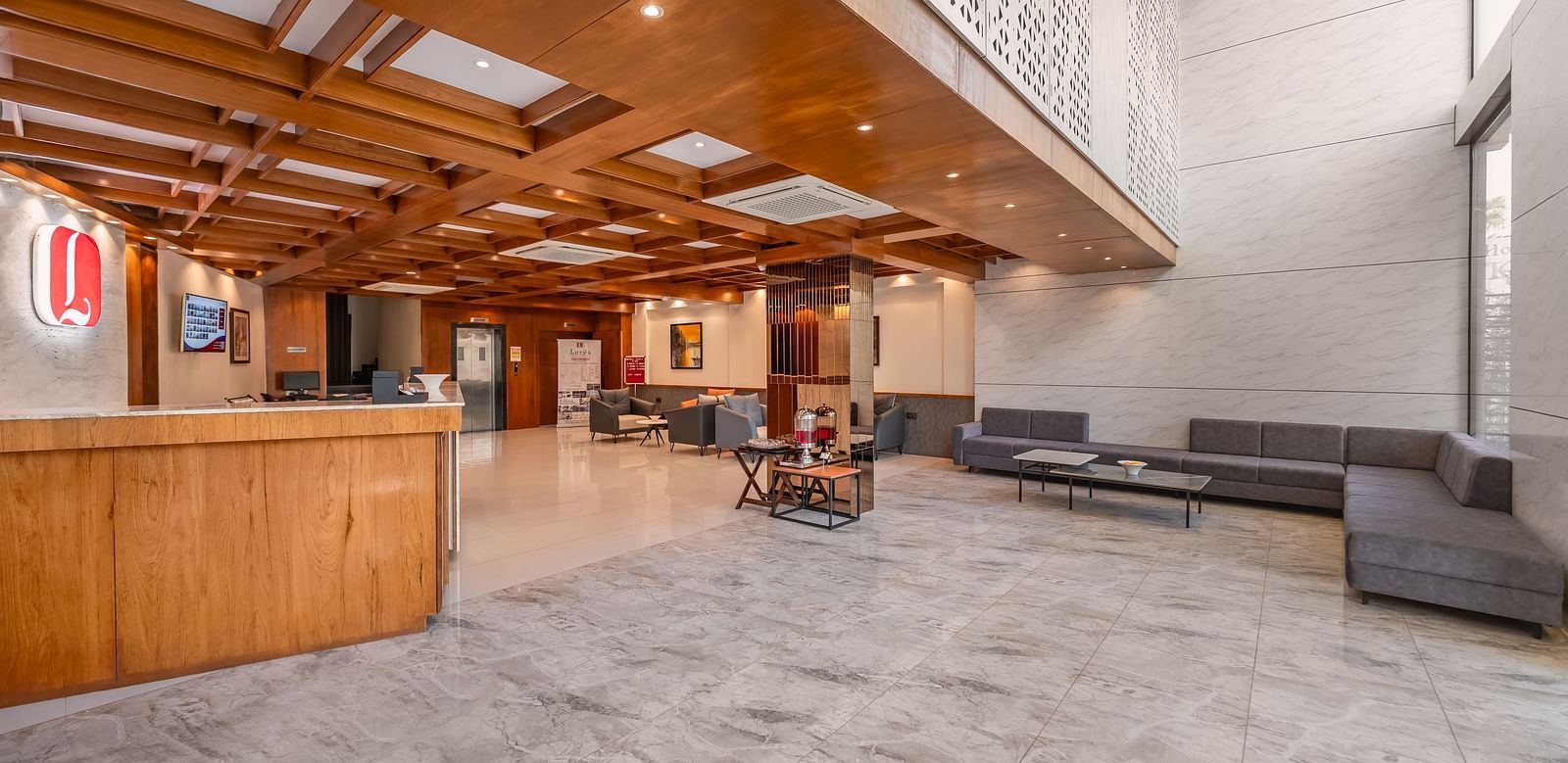 A spacious lobby features a wooden reception desk, lounge seating, and a high ceiling with wooden panels - Lords Eco Inn Ambaji.