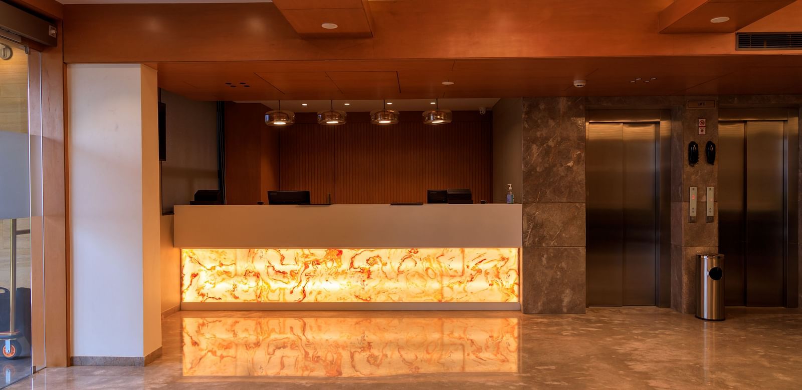 The warmly lit reception area of what appears to be Lords Eco Inn Apple Gate features a modern front desk, marble flooring, and elevators.