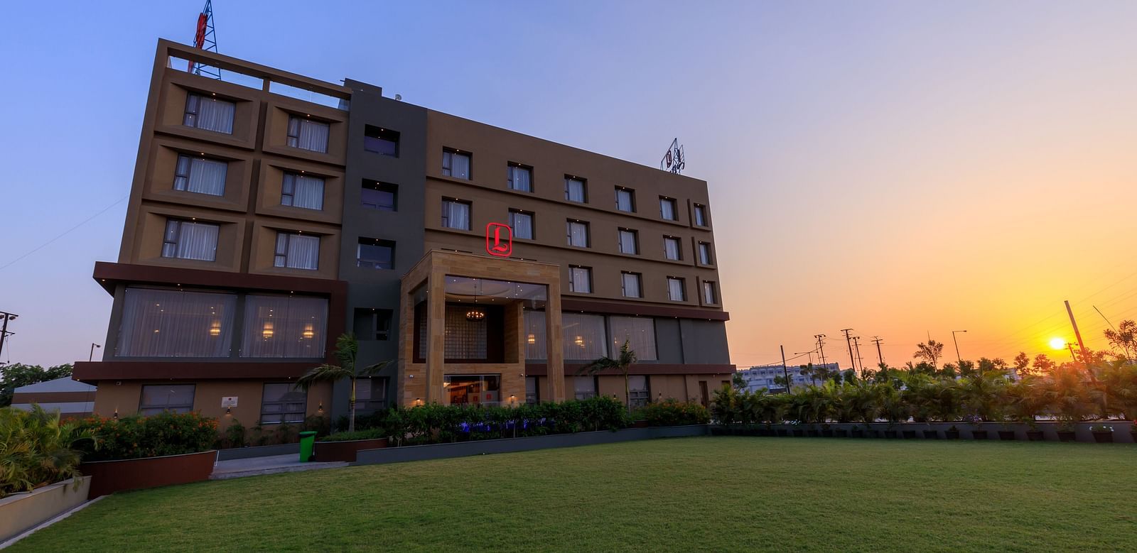 Facade of Lords Eco Inn Apple Gate hotel shown at dusk with the sun setting in the background, illuminating the modern building and green lawn.