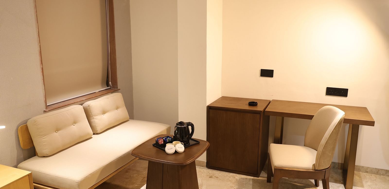 A well lit Deluxe Room at Lords Eco inn Jamnagar Maheshwari Nagar featuring a sofa bed writing desk and coffee table.