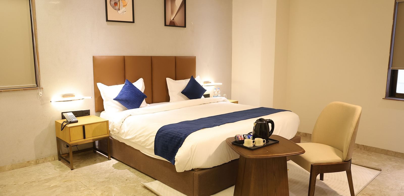 A spacious Deluxe Room at Lords Eco inn Jamnagar Maheshwari Nagar with a large bed two bedside tables and modern artwork.